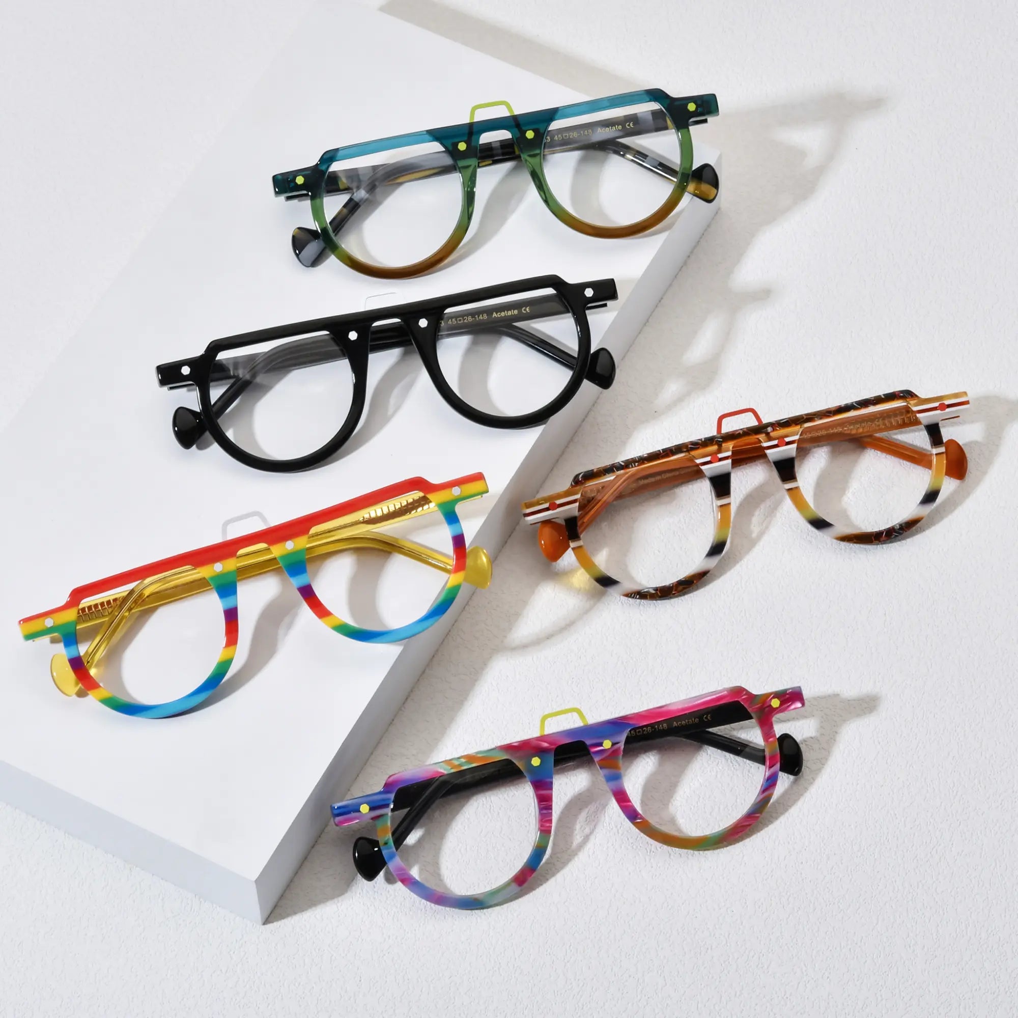 Top-down view of five VoyueLens™ VL19383 round eyeglass variants laid out on a white background, showcasing color options including Lime Tortoiseshell, Charcoal Black, Rainbow Stripe, Amber Stripe, and Rainbow Rush